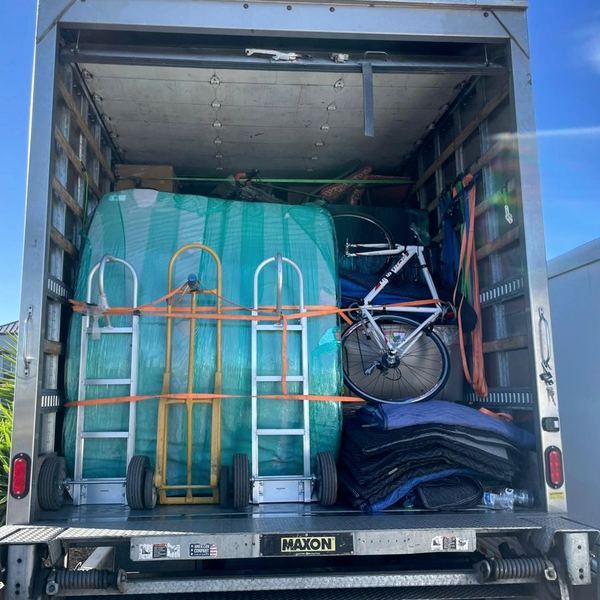 Loaded truck at the liftgate: shrink-wrapped goods, dollies and folded blankets strapped in